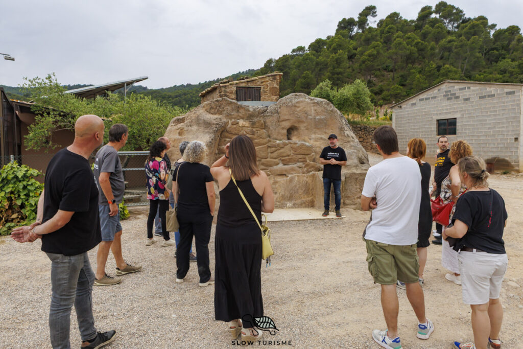 Grup de persones escoltant el guia davant d'una tina de pedra seca al Celler Exibis, dins una experiència d’enoturisme sostenible al Pla de Bages