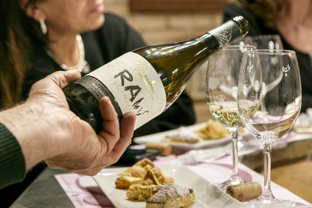 Mà servint vi blanc del Celler Collbaix al costat de croissants artesans en un tast.